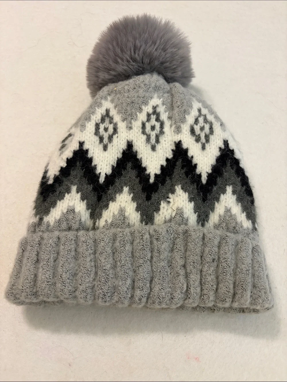 Gray knit beanie with a Fair Isle zigzag pattern and a fuzzy pom-pom on top.